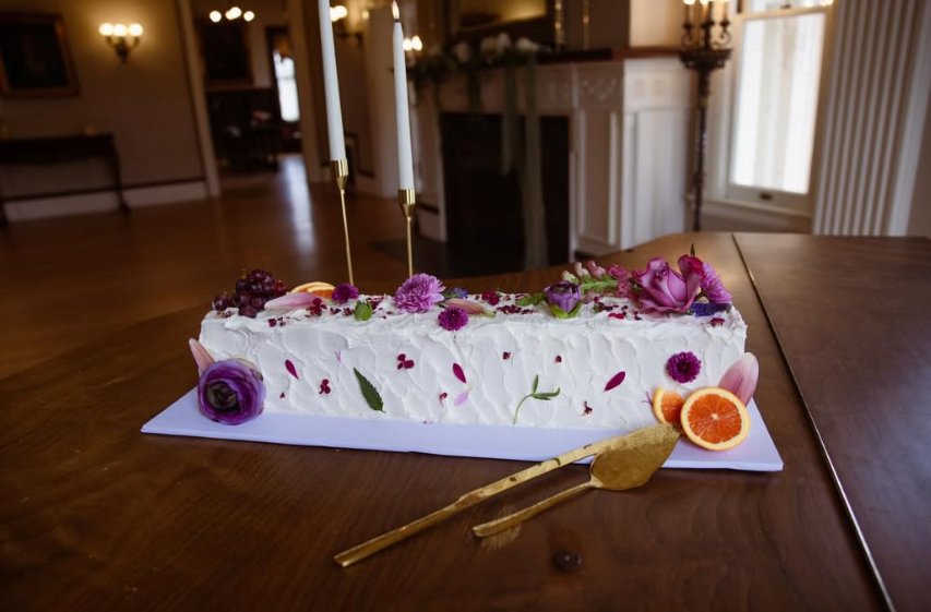 Rectangular wedding cake with purple wildflowers and citrus accents on a rustic table