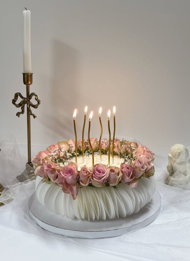 White pleated fondant cake crowned with fresh pink roses and lit gold candles